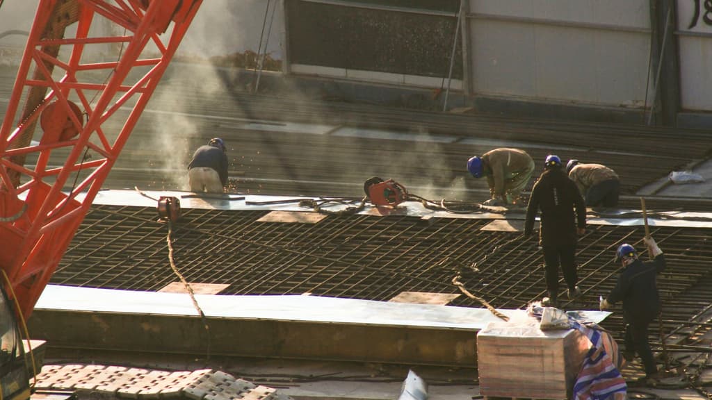 Construction crews welding on a rebar deck beside a crane, mid-job.